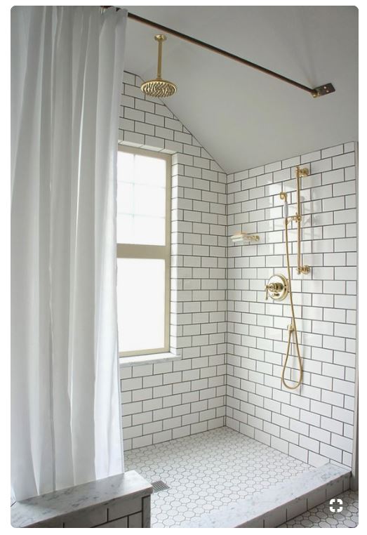 white subway tile shower with window brass fixture